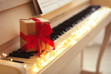 Gift box and fairy lights on piano keys, space for text. Christmas music