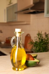 Photo of Fresh avocado and jug of cooking oil on beige marble table in kitchen