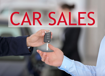 Image of Young salesman giving car key to client against blurred background, closeup