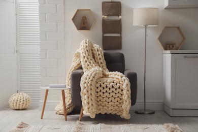 Photo of Comfortable armchair with chunky knit blanket in light living room