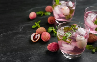 Delicious lychee cocktails with mint and fresh fruits on black table. Space for text
