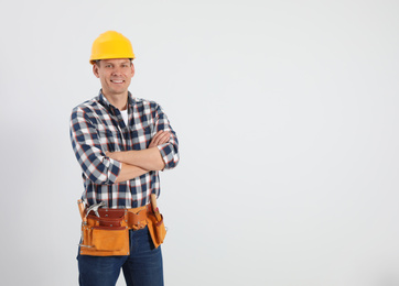 Photo of Handsome carpenter with tool belt on light background. Space for text