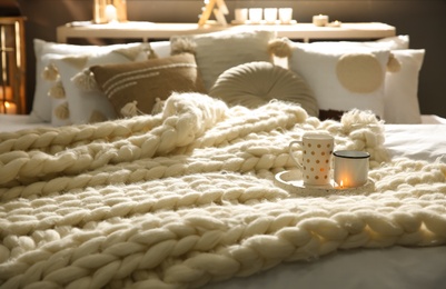 Cups and knitted blanket on bed in room. Interior decor