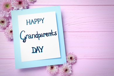 Beautiful flowers and card with phrase Happy Grandparents Day on pink wooden table, flat lay. Space for text