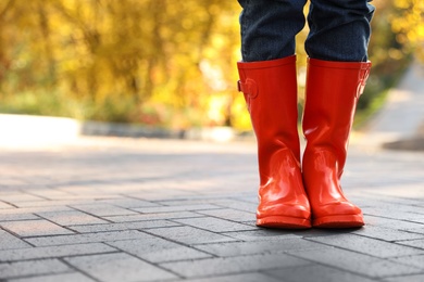 Woman wearing red rubber boots on paved street in park, closeup. Autumn walk