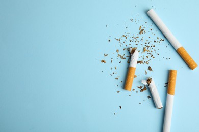 Photo of Broken and whole cigarettes on light blue background, flat lay with space for text. Quitting smoking concept