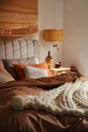 Bed with cozy knitted blanket and cushions indoors. Interior design