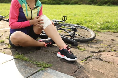 Young woman with injured knee near bicycle outdoors, closeup