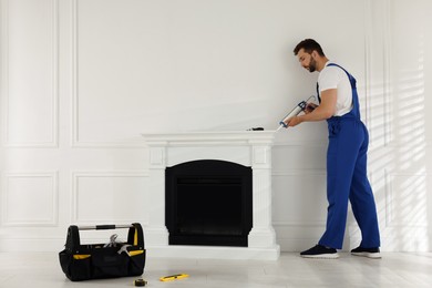 Professional technician sealing electric fireplace with caulk near white wall in room