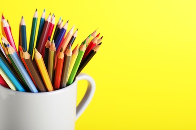 Colorful pencils in light cup on yellow background, closeup. Space for text