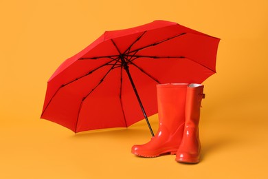 Open red umbrella and rubber boots on yellow background