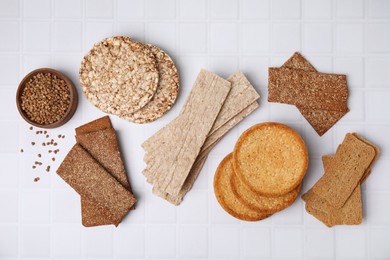 Rye crispbreads, rice cakes and rusks on white checkered table, flat lay