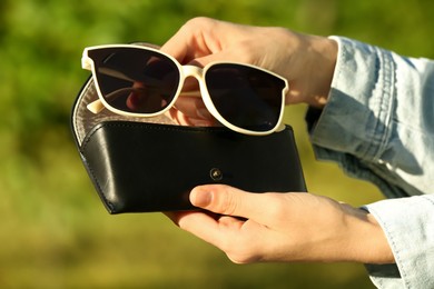 Woman holding sunglasses and case outdoors on sunny day, closeup