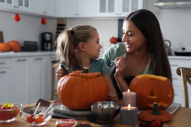 Mother and daughter making pumpkin jack o'lantern at table in kitchen. Halloween celebration