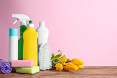 Photo of Spring cleaning. Detergents, tools and flowers on wooden table against pink background. Space for text
