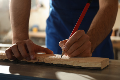 Professional carpenter making mark on wooden board in workshop, closeup