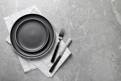 New dark plates, cutlery and napkin on light grey marble table, flat lay. Space for text