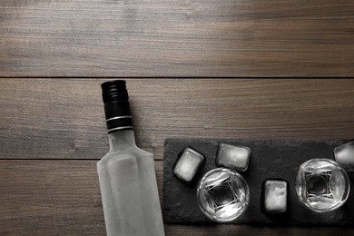 Bottle of vodka, shot glasses and ice cubes on wooden table, flat lay. Space for text