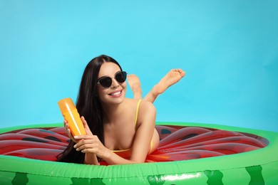 Young woman with sun protection cream on inflatable mattress against light blue background