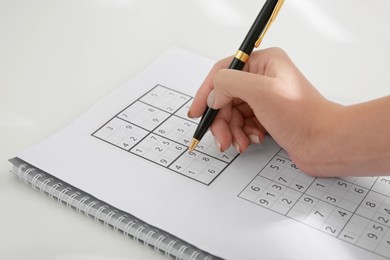 Woman solving sudoku puzzle at white table, closeup