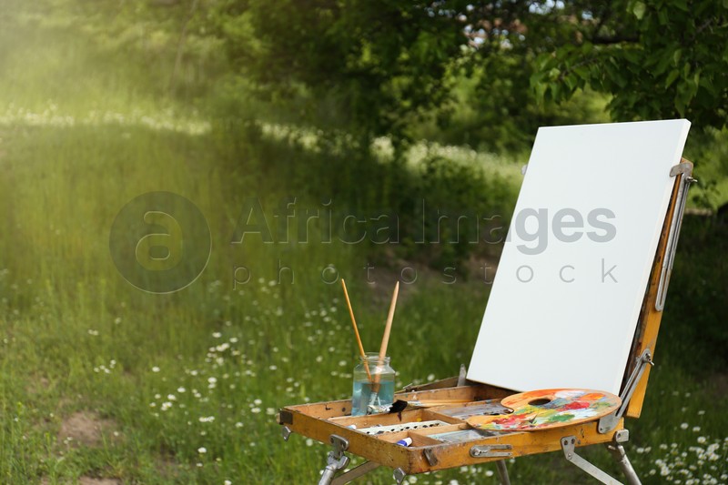 Easel with blank canvas and painting equipment in picturesque countryside
