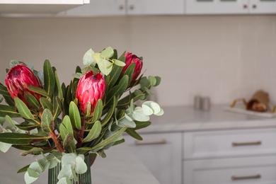 Photo of Bouquet of beautiful protea flowers and eucalyptus branches in kitchen interior, closeup. Space for text