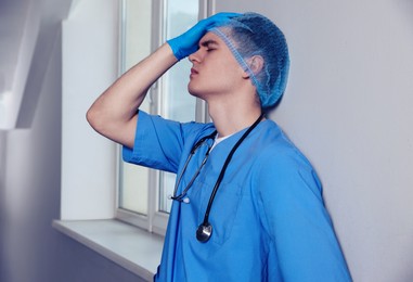 Photo of Stressed doctor near grey wall in hospital hallway