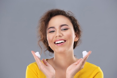 Beautiful young woman with problem skin applying anti acne cream on grey background
