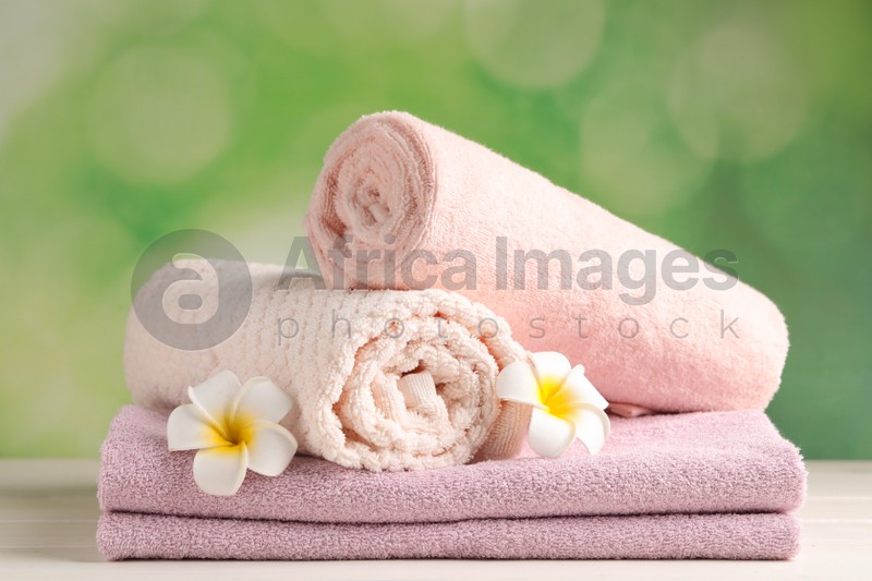 Photo of Soft folded towels and plumeria flowers on white wooden table