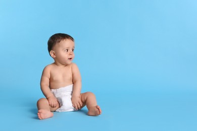 Cute baby in dry soft diaper sitting on light blue background. Space for text