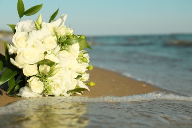 Beautiful wedding bouquet on sandy beach near sea. Space for text