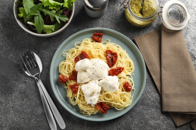 Delicious spaghetti with burrata cheese and sun dried tomatoes served on grey table, flat lay