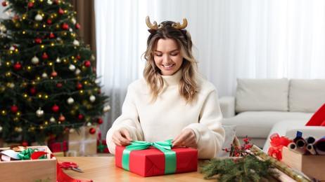 Beautiful young woman wrapping Christmas gift at home