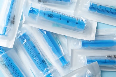 Packed disposable syringes with needles on light blue background, top view
