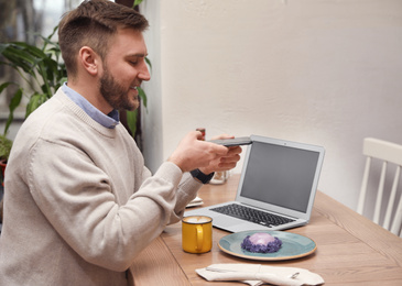 Male blogger taking photo of dessert and coffee at table in cafe