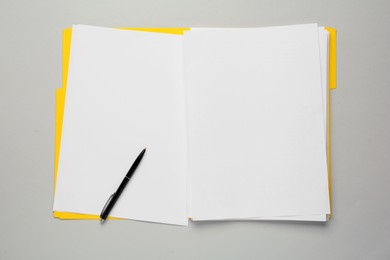 Yellow file with blank sheets of paper and pen on light grey background, top view. Space for design