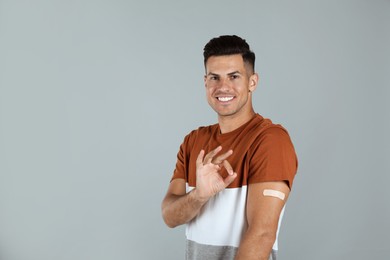 Vaccinated man with medical plaster on his arm showing okay gesture against grey background