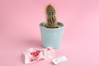 Cactus, suppository and sheet of toilet paper with blood on pink background. Hemorrhoid problems