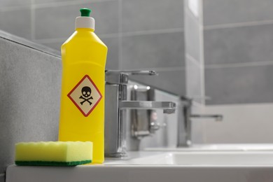 Photo of Bottle of toxic household chemical with warning sign and scouring sponge in bathroom, space for text