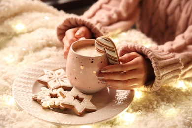 Woman with cup of hot drink and Christmas cookies at home, closeup