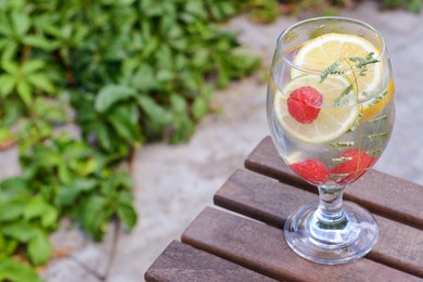 Photo of Delicious refreshing lemonade with raspberries on wooden table outdoors, space for text