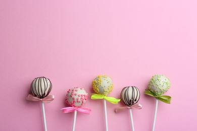 Different tasty cake pops on light pink background, flat lay. Space for text