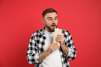 Photo of Young man eating delicious shawarma on red background