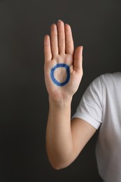 Photo of Woman showing blue circle drawn on palm against dark grey background, closeup. World Diabetes Day