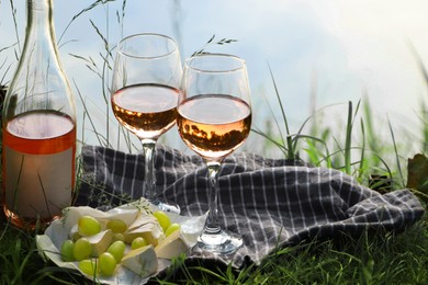 Delicious rose wine, cheese and grapes on picnic blanket near lake, closeup