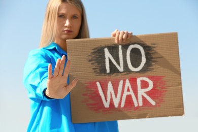 Photo of Sad woman holding poster with words No War and showing stop gesture outdoors