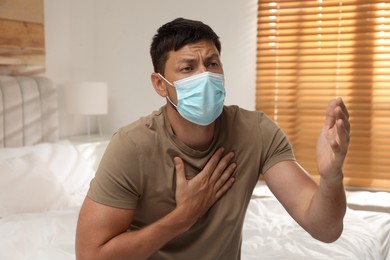 Man with medical mask suffering from pain during breathing in bedroom
