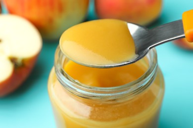 Spoon with healthy baby food over glass jar on turquoise table, closeup