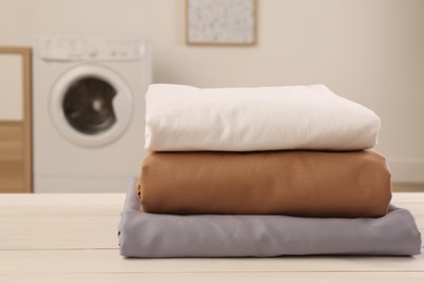 Stack of clean bed linens on white wooden table in laundry room