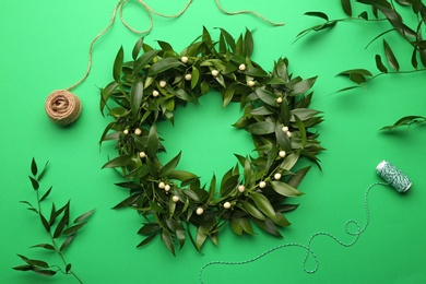 Beautiful handmade mistletoe wreath and florist supplies on green background, flat lay. Traditional Christmas decor